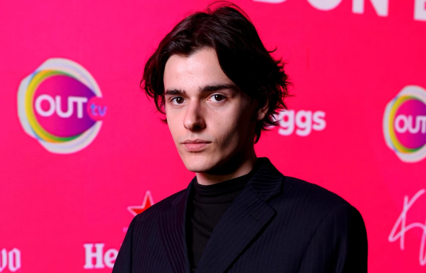 Marko Bošnjak - reprezentant Chorwacji w Eurowizji 2025 Młody mężczyzna o ciemnych włosach ubrany w elegancki, ciemny strój na tle różowej ścianki z logotypami sponsorów i partnerów medialnych.