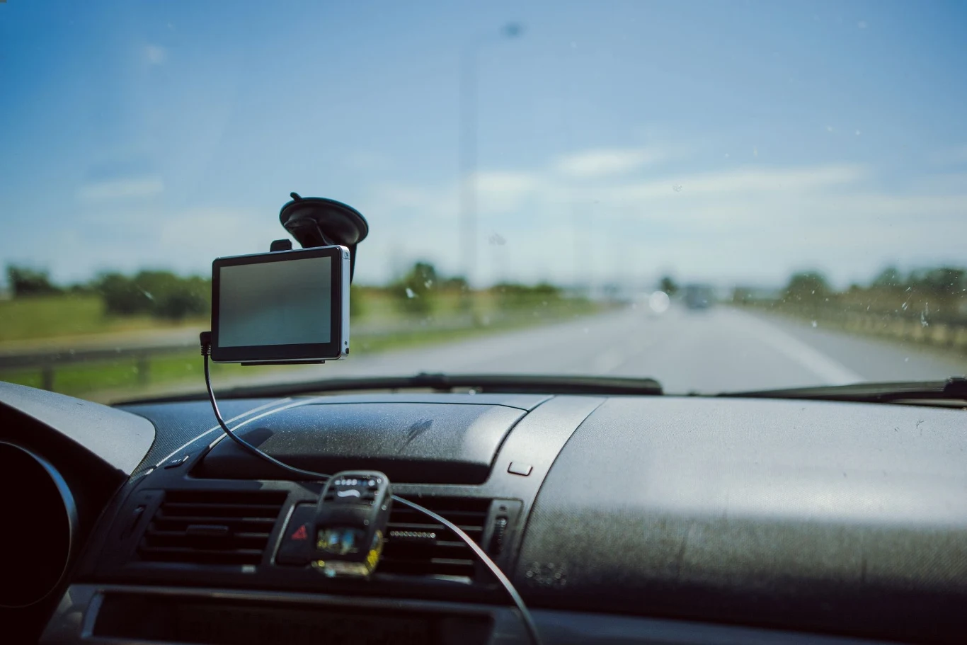Urządzenie GPS zamocowane na przedniej szybie samochodu pokazujące trasę podróży, z widoczną szeroką drogą w otwartym terenie za szybą.