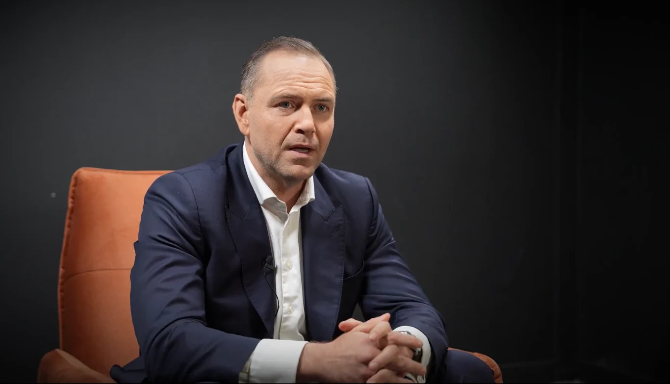 Karol Nawrocki odpowiada Rafałowi Trzaskowskiemu. Ma dla niego kopertę Elegancko ubrany mężczyzna siedzi w pomarańczowym fotelu na ciemnym tle, wyglądając poważnie i profesjonalnie, jakby podczas ważnej rozmowy lub wywiadu.