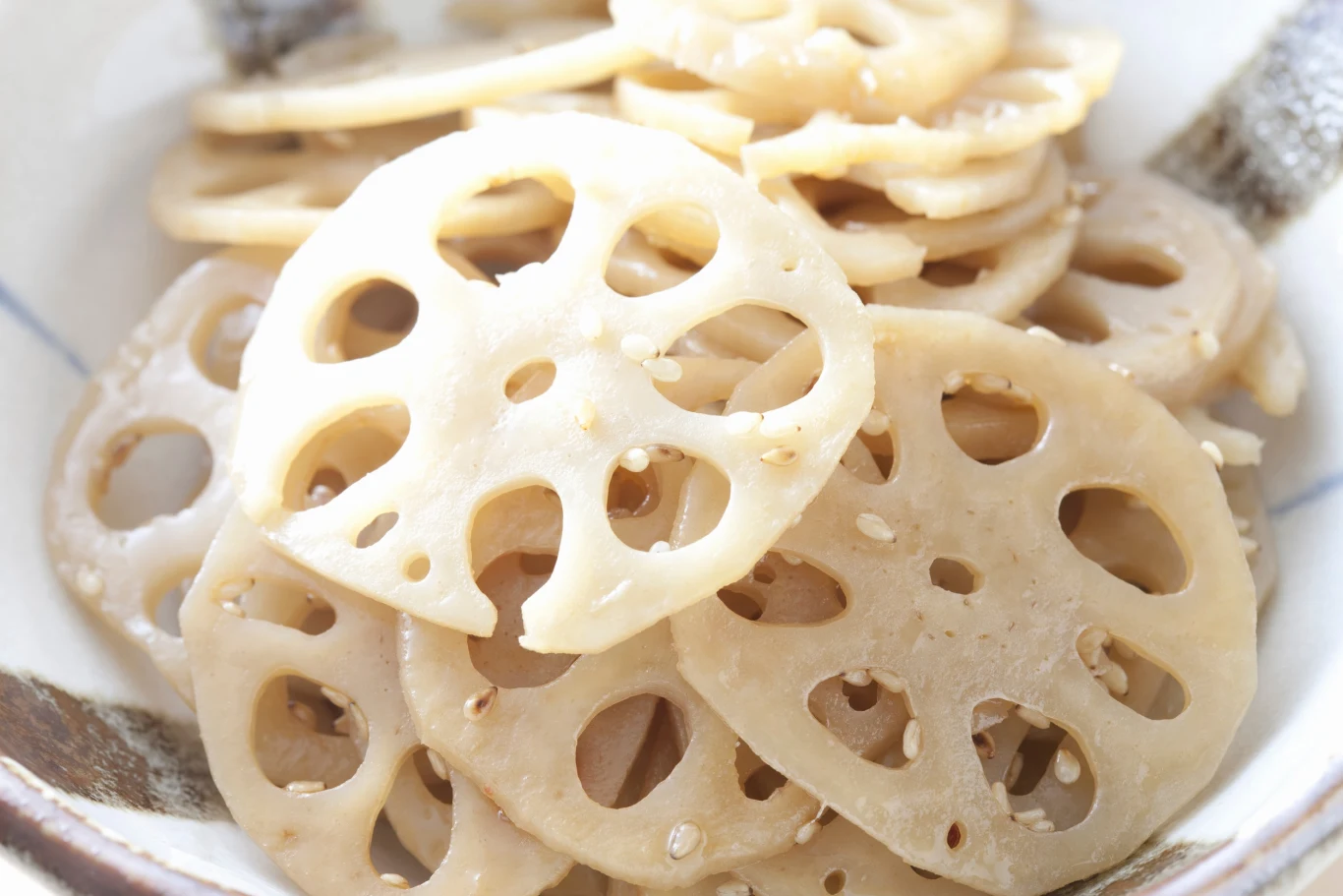 Korzeń lotosu to warzywo o nietypowym kształcie i cennych właściwościach dla zdrowia Plasterki korzenia lotosu ułożone w białej misce, widoczny charakterystyczny wzór otworów w każdym z nich.