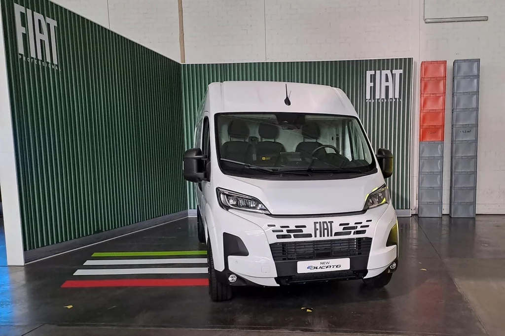 Fiat Ducato to najchętniej kupowany samochód wśród prywatnych osób w Niemczech w kwietniu 2025 r. Biały samochód dostawczy Fiat stoi w pomieszczeniu na tle ściany w zielono-szarych panelach. Na ziemi widoczne są pasy w kolorach flagi Włoch. Na ścianie znajduje się logo producenta.