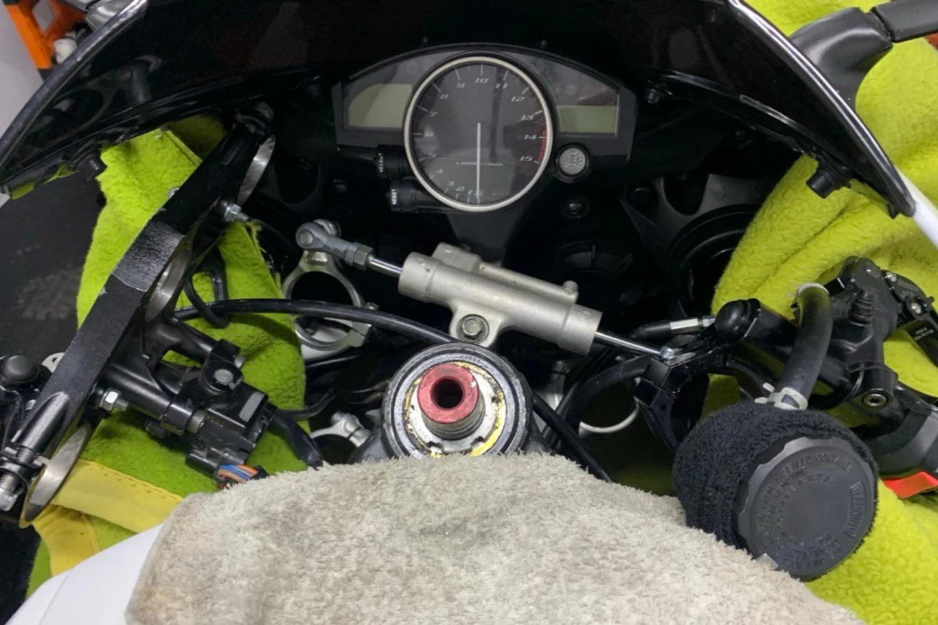 Panel sterowania motocyklu wyścigowego, z widocznymi elementami mechanicznymi i elektronicznymi. W centrum znajduje się prędkościomierz, otoczony różnymi kontrolkami i przełącznikami, a wokół niego rozmieszczone są różne przewody i uchwyty.
