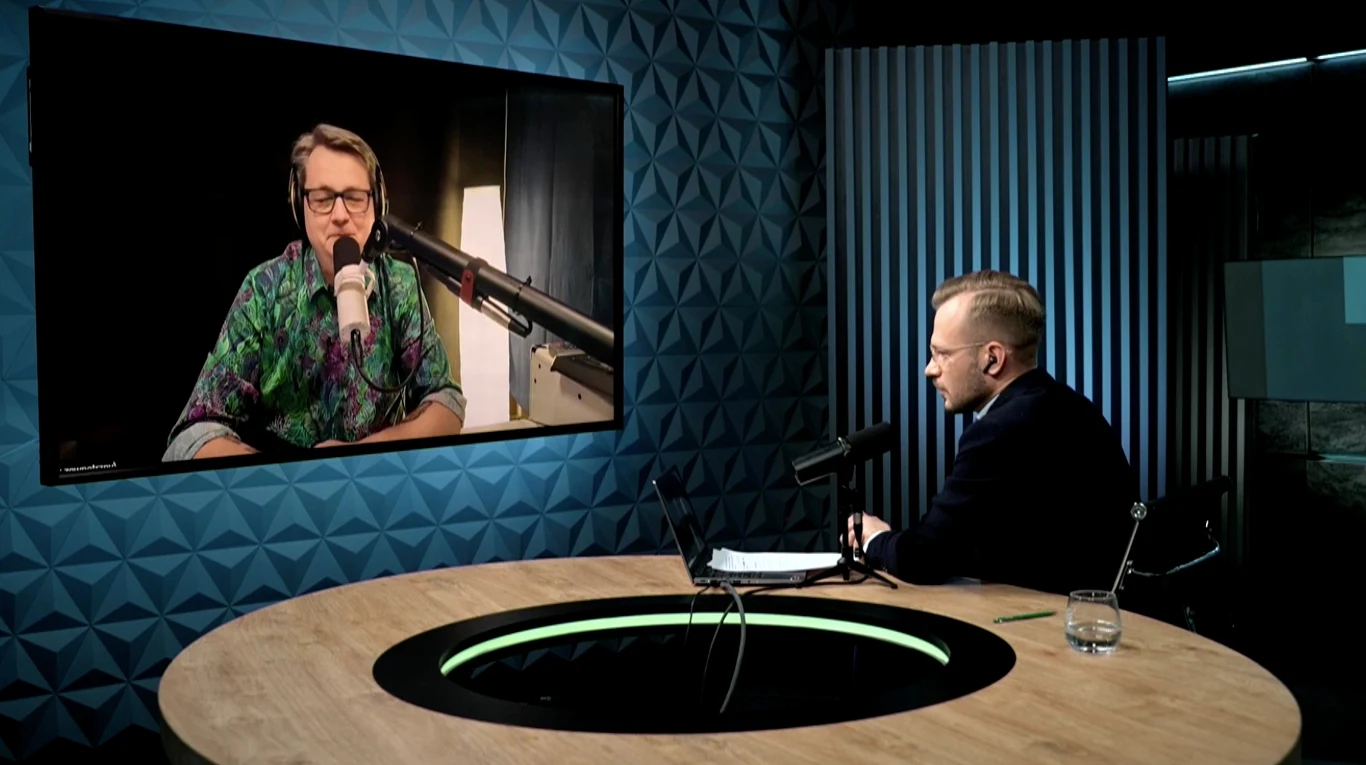 Podcast Geekweeka. Drugi Polak leci w kosmos. Dwóch mężczyzn prowadzi rozmowę online. Jeden siedzi przy okrągłym stole w studio, drugi pojawia się na dużym ekranie. Obaj używają mikrofonów, a klimat jest profesjonalny.