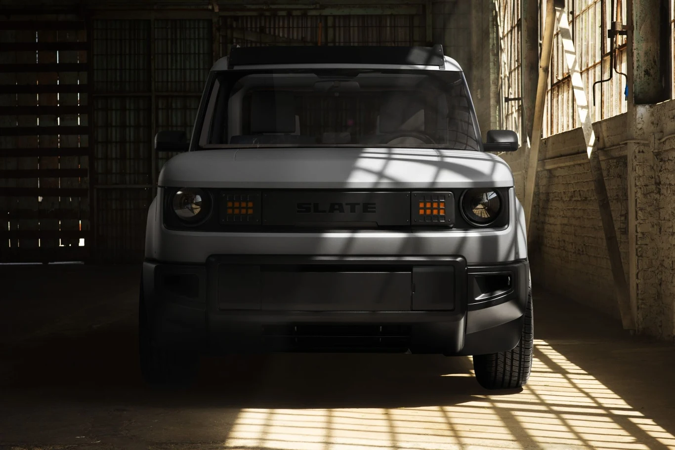 Samochód terenowy w ciemnym garażu, oświetlony światłem wpadającym przez okna. Duża maska i charakterystyczne reflektory dodają mu masywnego wyglądu.