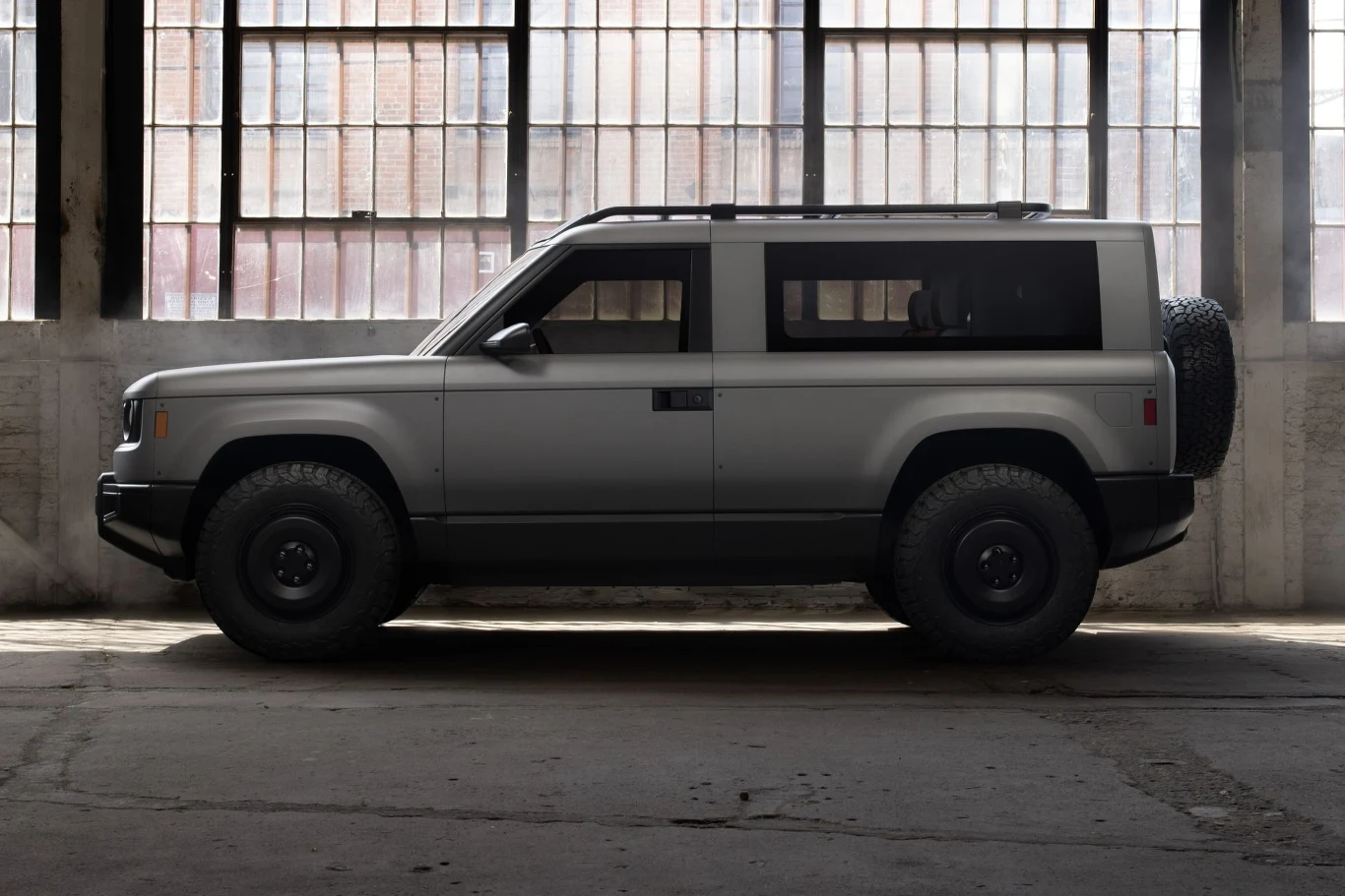 Szary samochód terenowy w opuszczonym magazynie, z dużymi oknami w tle. Pojazd stoi na betonowej podłodze, tworząc kontrast z przemysłowym otoczeniem.