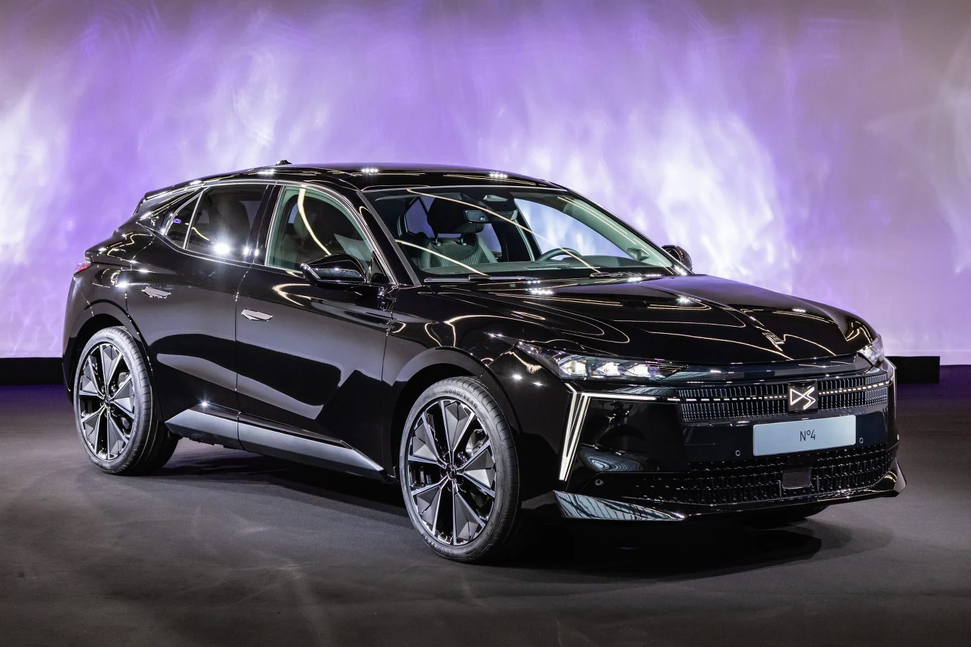 Nowoczesny, czarny SUV o eleganckiej i aerodynamicznej sylwetce, stojący na tle jasnego, fioletowego oświetlenia. Połyskujący lakier podkreśla dynamiczne kształty samochodu oraz duże, aluminiowe felgi.