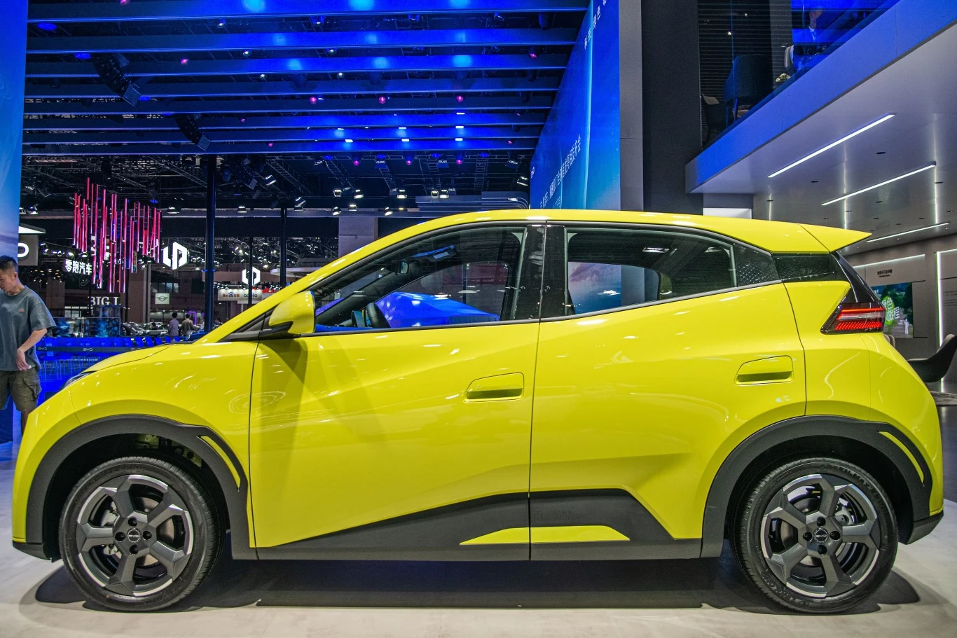 Jasnożółty kompaktowy samochód na targach motoryzacyjnych, ustawiony na tle nowoczesnych świateł i technologicznych instalacji.