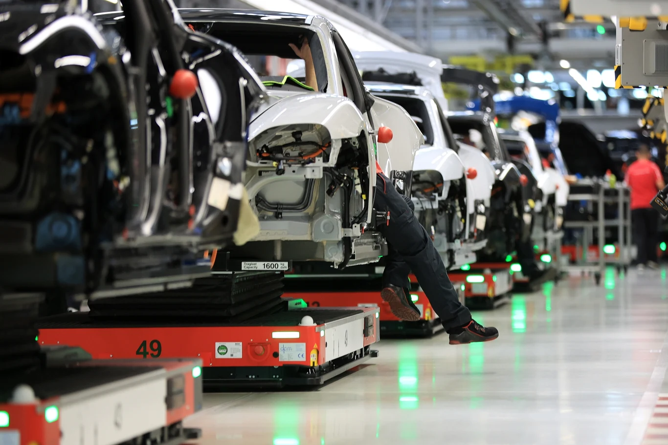 Porsche w coraz większym kryzysie. Elektryfikacja okazała się błędem Linia produkcyjna samochodów, gdzie widać częściowo zmontowane pojazdy i jednego pracownika wykonującego prace montażowe w fabryce. Jasna hala z nowoczesną technologią automatyki przemysłowej.