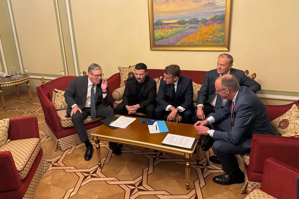 Liderzy "koalicji chętnych" podczas spotkania z prezydentem Wołodymyrem Zełenskim w Kijowie na początku maja Grupa pięciu mężczyzn w formalnych strojach siedzi wokół małego stołu w eleganckim pokoju, na stole leżą dokumenty. Obraz w tle przedstawia krajobraz z kwiatami.