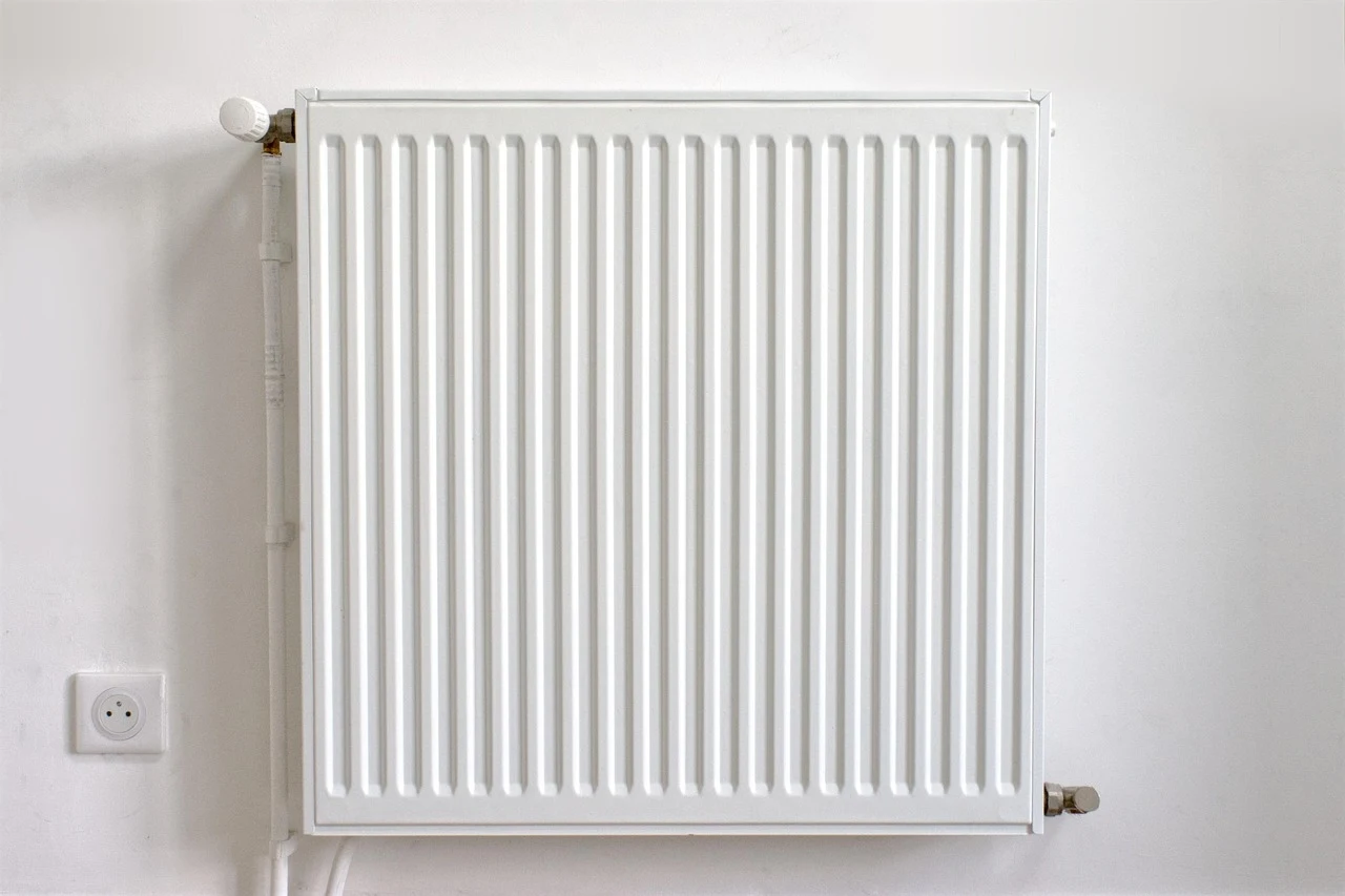 Biały grzejnik ścienny zamontowany na gładkiej ścianie, obok znajduje się gniazdko elektryczne.