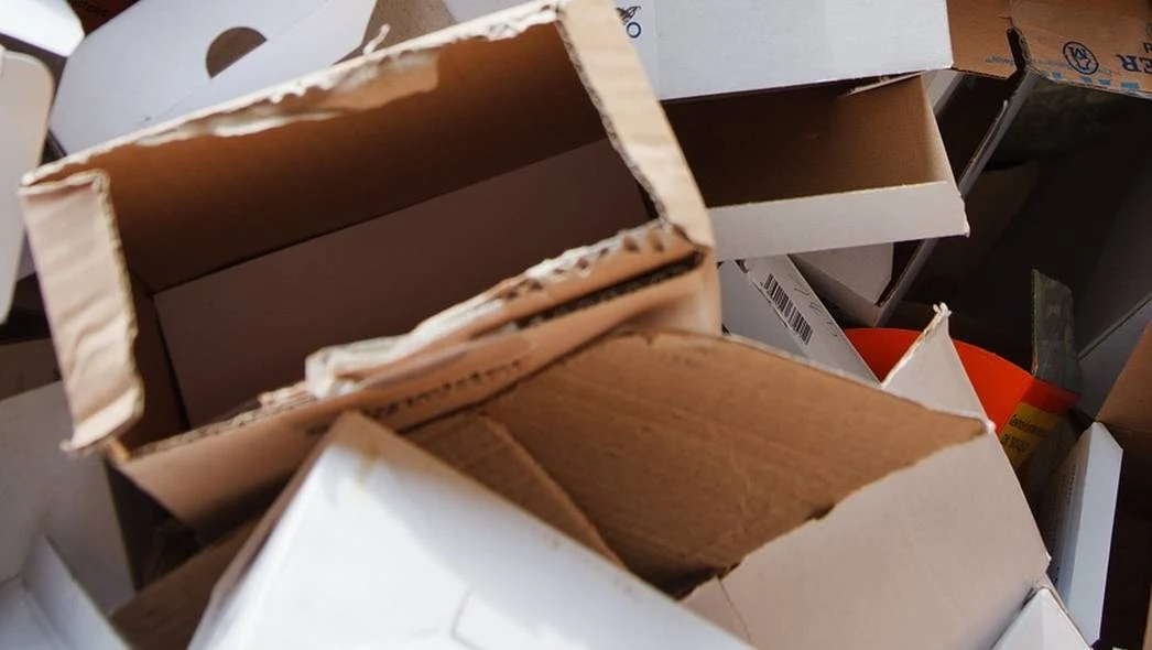 Stos zniszczonych kartonowych pudełek o różnych rozmiarach. Widoczne są oznaki zużycia, zagięcia i uszkodzenia. Pudełka leżą chaotycznie jedno na drugim, tworząc nieuporządkowaną kompozycję.