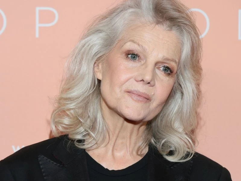 Katarzyna Butowtt wciąż po latach zachwyca na wybiegach Osoba dojrzała o siwych włosach, stojąca na pomarańczowym tle. Ubrana w ciemną marynarkę.