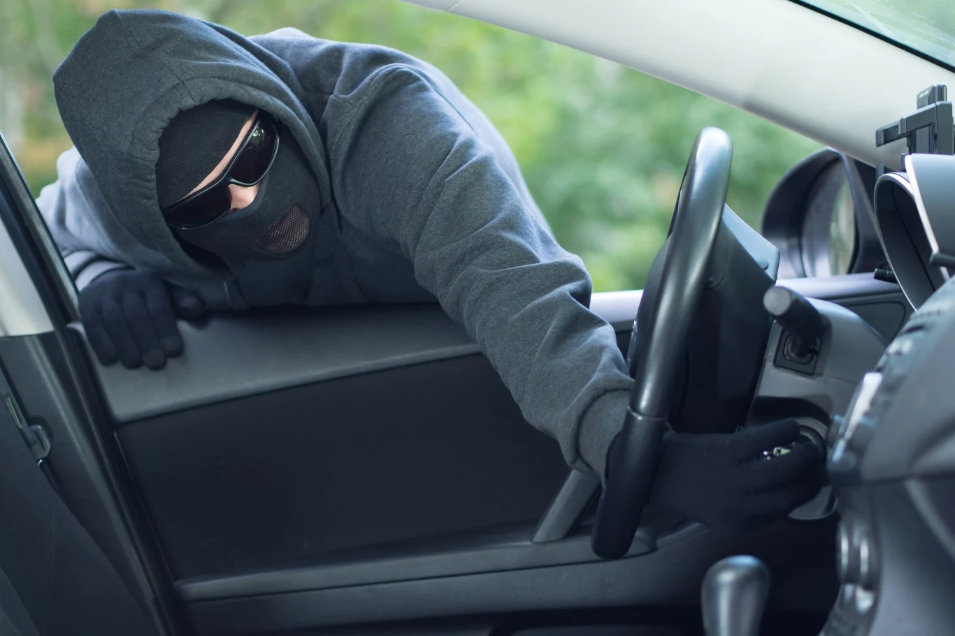Zostawienie kluczyków w samochodzie również może być karalne. Mężczyzna w kapturze i okularach przeciwsłonecznych próbuje ukraść samochód, wsuwając rękę przez opuszczone okno do wnętrza pojazdu. Widać część kierownicy oraz deskę rozdzielczą.