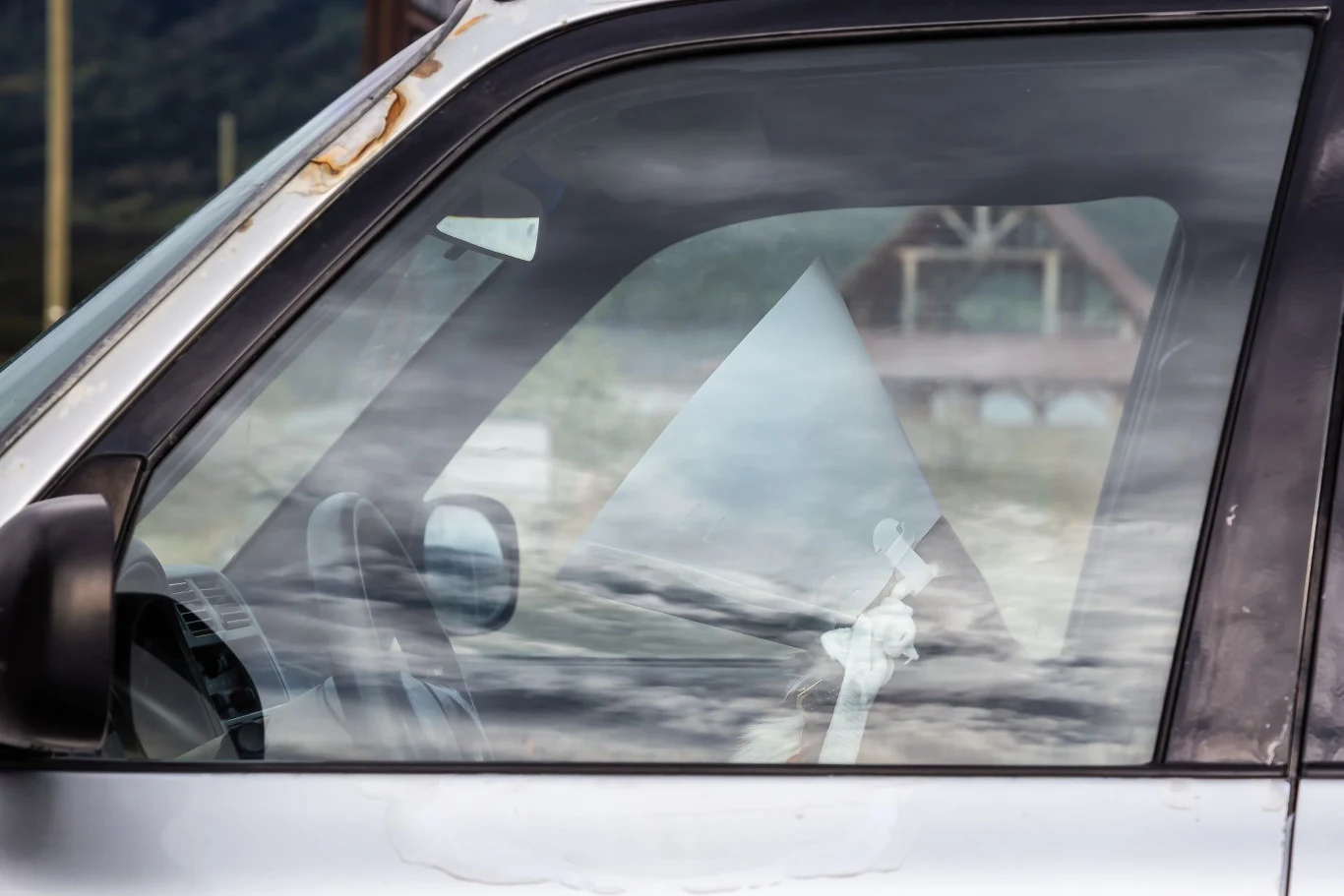 O surowości włoskich przepisów przekonał się kierowca z Turynu. Bok samochodu z widocznym bocznym lusterkiem i szybą, przez którą prześwituje krajobraz z górą i domem w tle. Odbicie na szybie dodaje głębi, tworząc mieszankę wnętrza auta i zewnętrznego widoku.