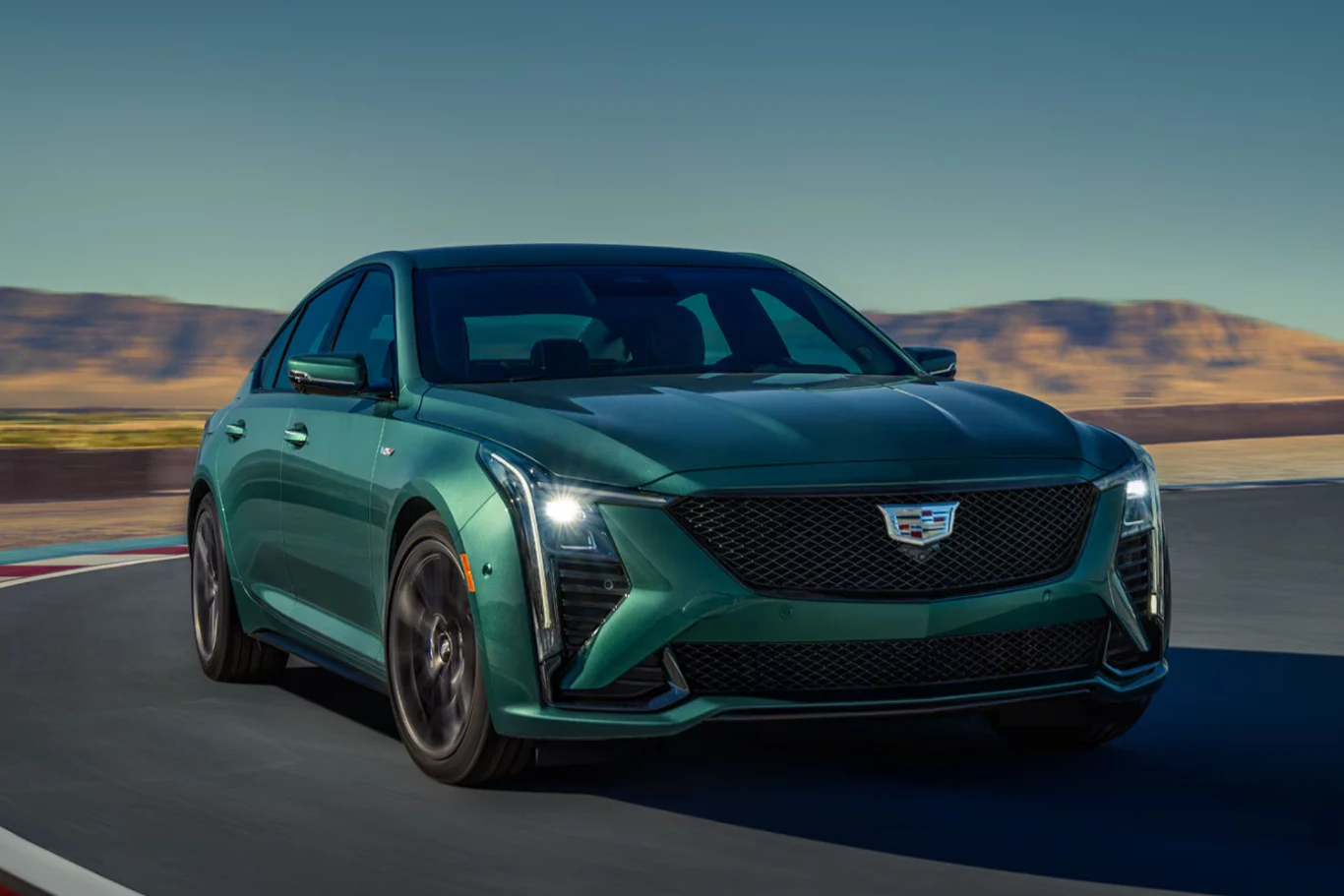 Cadillac CT5-V Blackwing to pocisk na czterech kołach. Jednostka V8 z kompresorem poraża mocą. Zielony samochód marki Cadillac na torze wyścigowym. Elegancki i nowoczesny design, czarny grill i wyraziste reflektory podkreślają sportowy charakter auta.