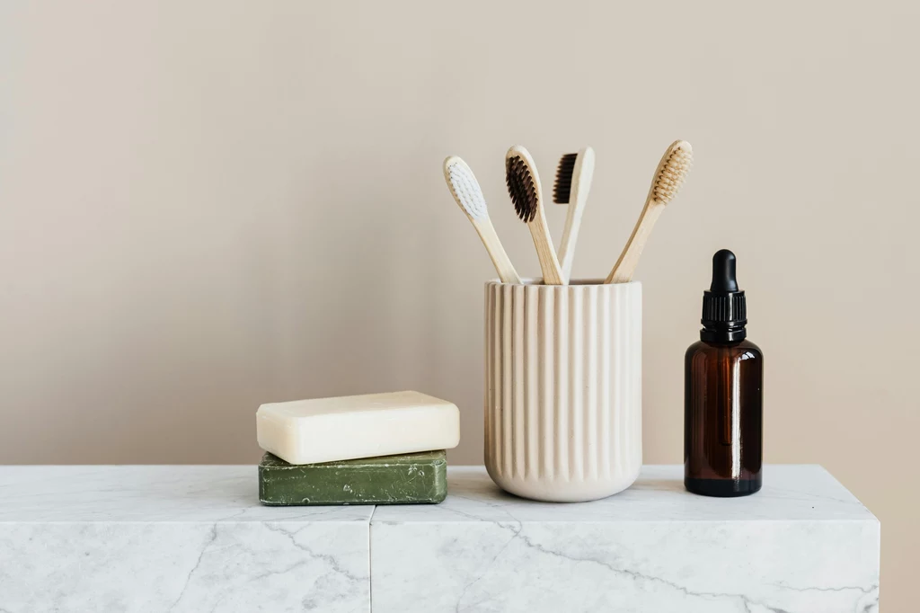 Fot.pexels.com/ Photo By: Kaboompics.com Ceramiczny kubek z czterema szczoteczkami do zębów, dwie kostki mydła i butelka z dozownikiem nawiązująca do stylu minimalistycznego. Przedmioty ustawione na marmurowym blacie w neutralnych kolorach.