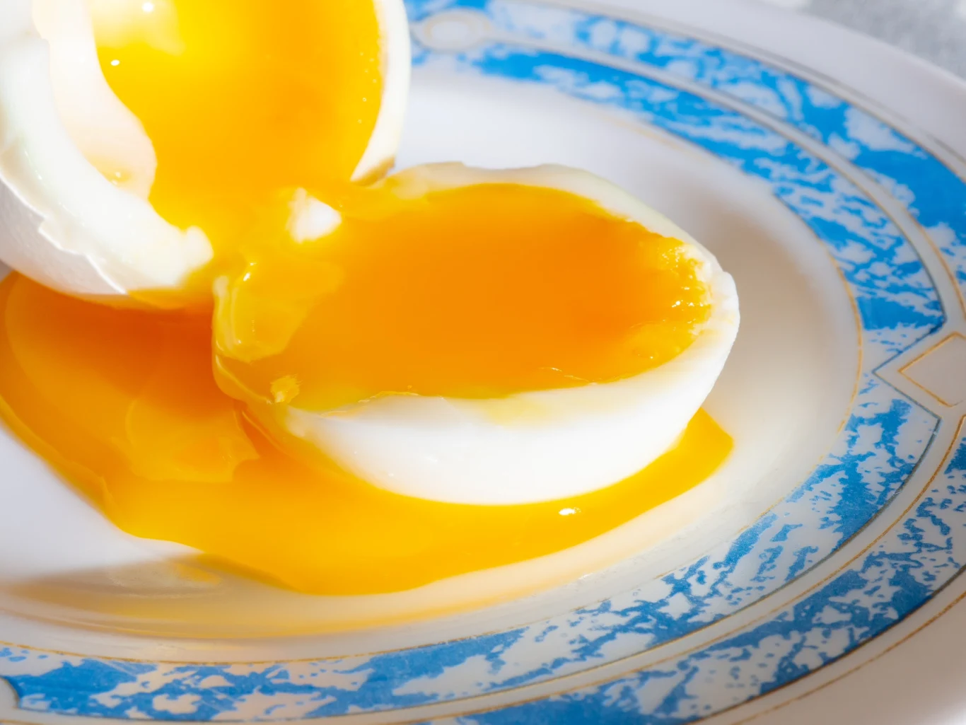 Jajko na miękko z płynącym żółtkiem na białym i niebieskim talerzu.
