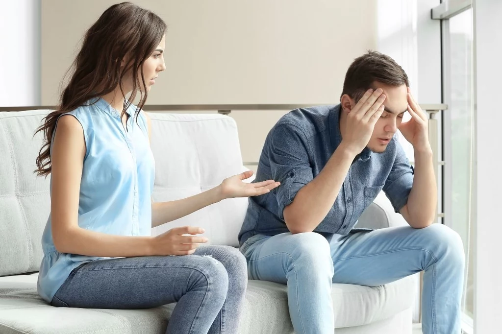 Umniejszanie emocjom drugiej osoby powoduje stopniowe odsuwanie się jej Mężczyzna i kobieta siedzą na kanapie w domowym wnętrzu. Kobieta gestykuluje, jakby próbowała coś wyjaśnić lub dyskutować, a mężczyzna trzyma głowę w dłoniach, sprawiając wrażenie zmartwionego lub zestresowanego.