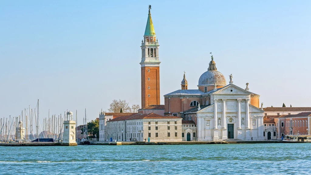 Jedna z wysp Laguny Weneckiej Malowniczy widok na kościół San Giorgio Maggiore w Wenecji, z charakterystyczną wieżą i kopułą. W tle widać spokojną wodę i cumujące łodzie, a architektura zachwyca renesansowym stylem.