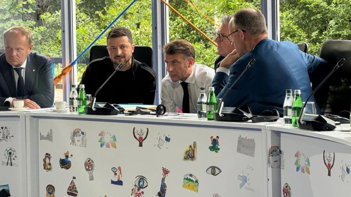 Donald Tusk, Wołodymyr Zełenski, Emmanuel Macron, Keir Starmer, Friedrich Merz podczas rozmów na szczycie EPC Grupa mężczyzn siedzących przy stole ozdobionym rysunkami, dyskutują w eleganckich strojach przy otwartym oknie z widokiem na zieleń.