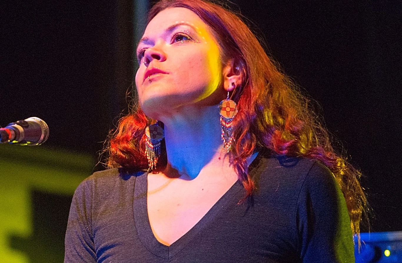 Zia McCabe (The Dandy Warhols) w 2014 roku Kobieta przy mikrofonie, zwrócona twarzą do góry, dobrze oświetlona, z długimi, rudymi włosami i ozdobnymi kolczykami. Jej wyraz twarzy jest skupiony.