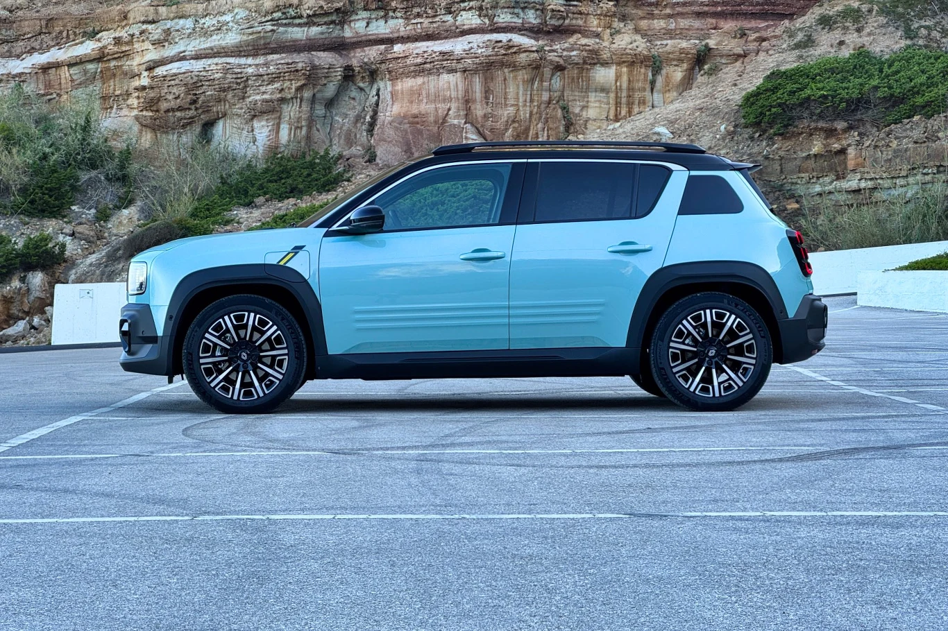 Samochód osobowy w kolorze niebieskim zaparkowany na tle skalistego wzgórza i bujnej roślinności.