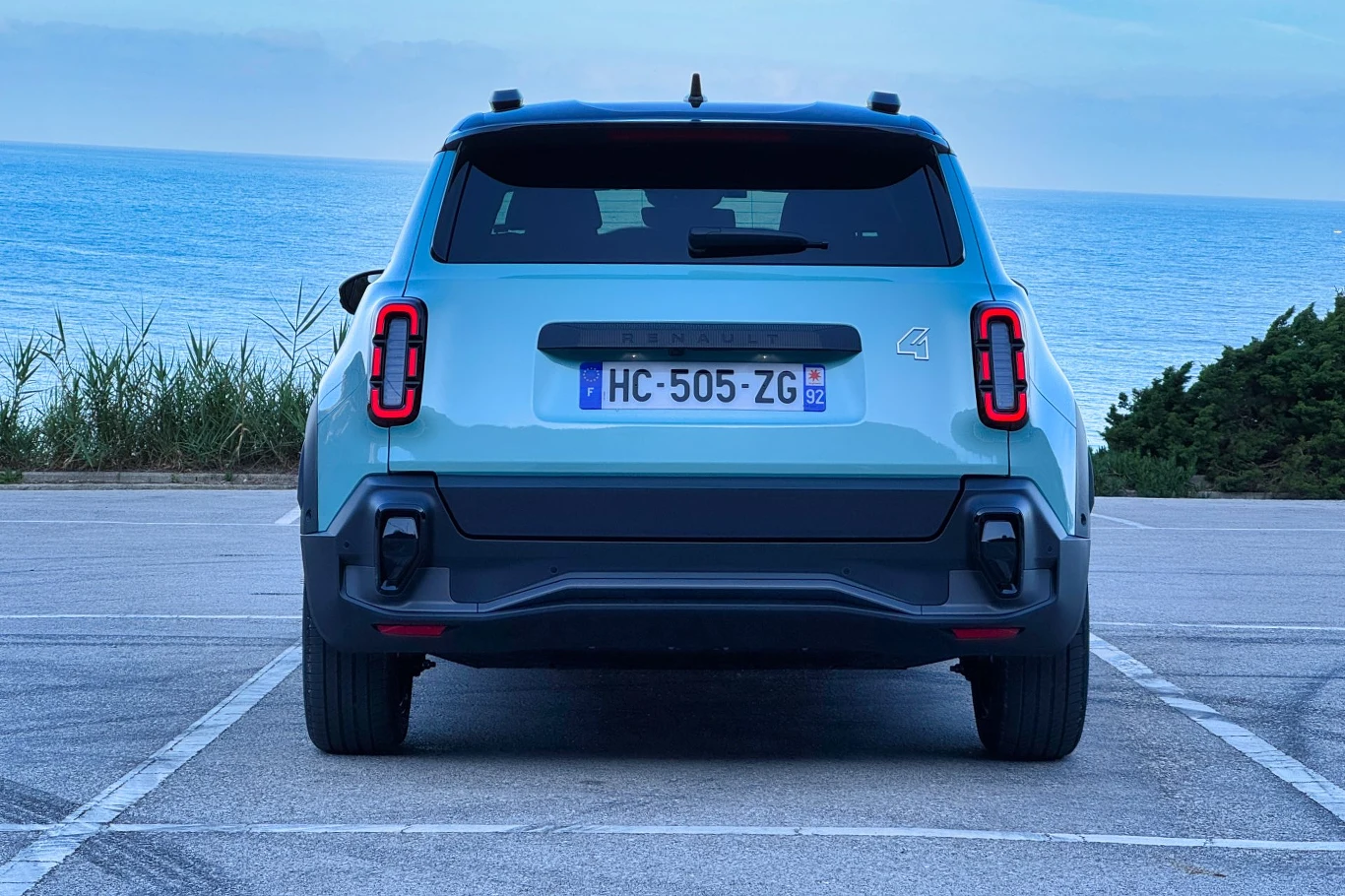 Tył niebieskiego samochodu zaparkowanego na tle morza. Widać numer rejestracyjny HC-505-ZG. W okolicy znajdują się niewielkie zarośla i krzewy.