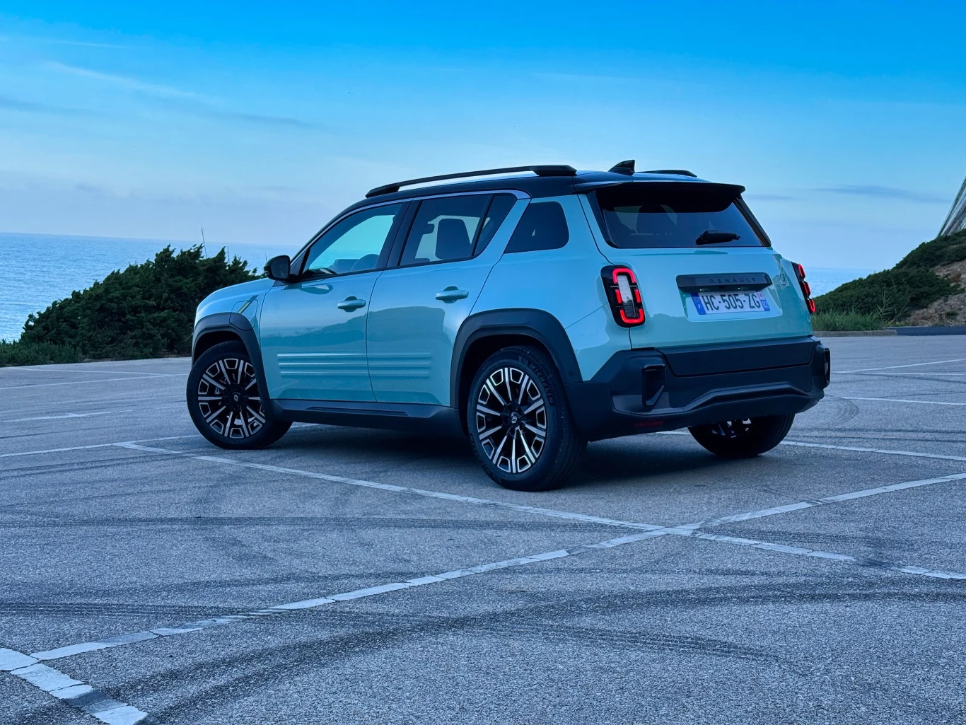 Samochód SUV na pustym parkingu przy wybrzeżu, w tle widać morze i błękitne niebo. Pojazd w kolorze niebieskim, z ciemnymi szybami i czarnymi elementami wykończenia.