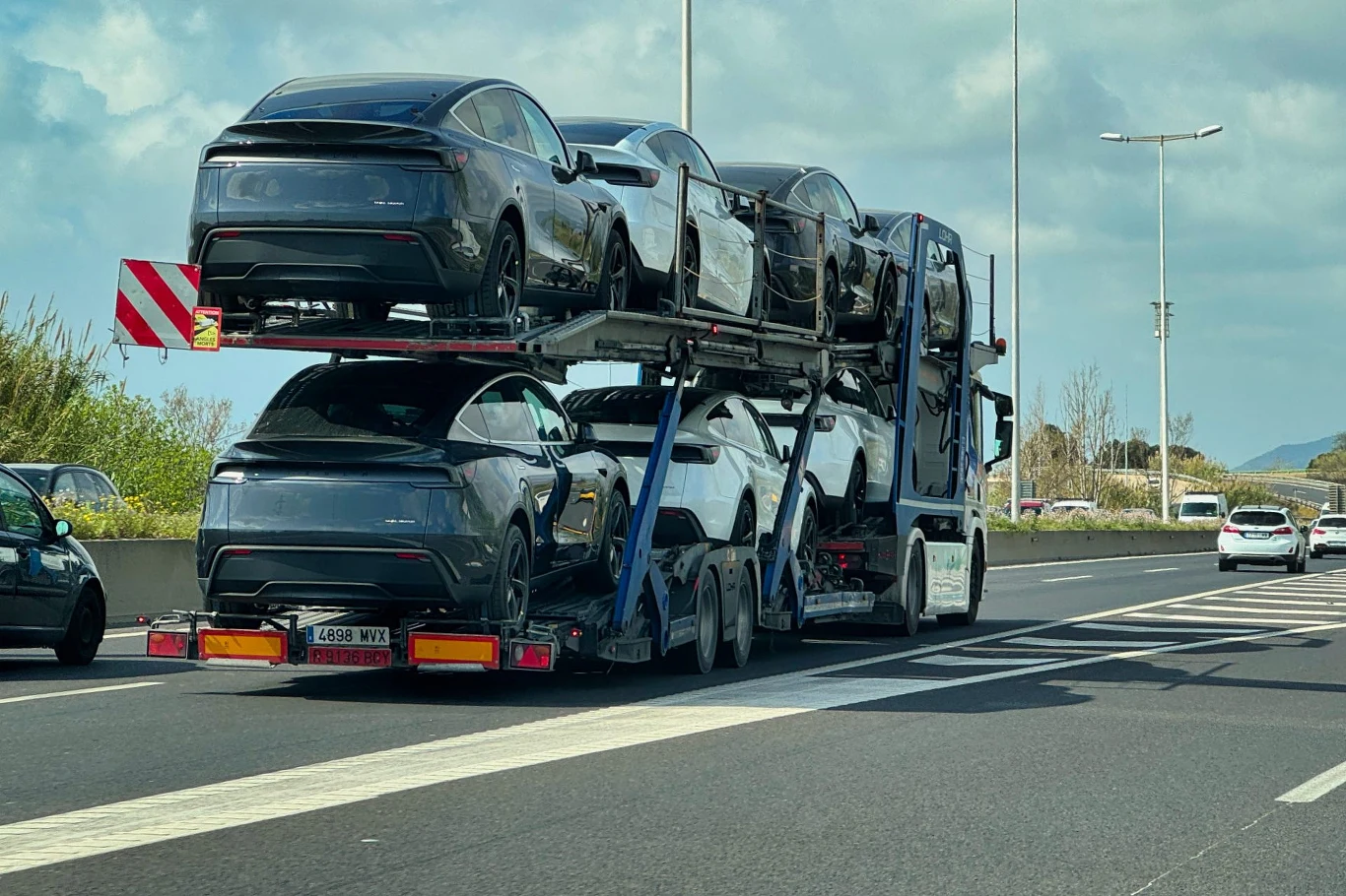 Samochody leasingowane w Polsce często trafiają do zagranicznych wypożyczalni Samochody elektryczne na lawetach przewożone autostradą w słoneczny dzień. W tle widoczny jest krajobraz z drzewami i górami.