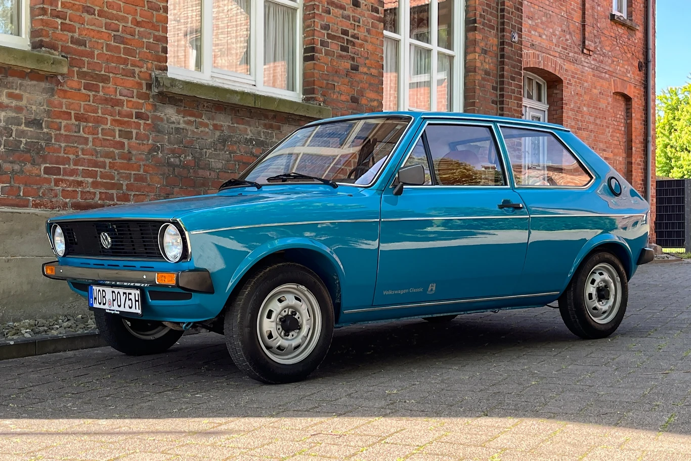 Volkswagen Polo kończy 50 lat. "Mały z zewnątrz. Duży w środku" Nieco retro niebieski samochód stojący na tle ceglanego budynku, z widocznymi krawędziami chodnika.