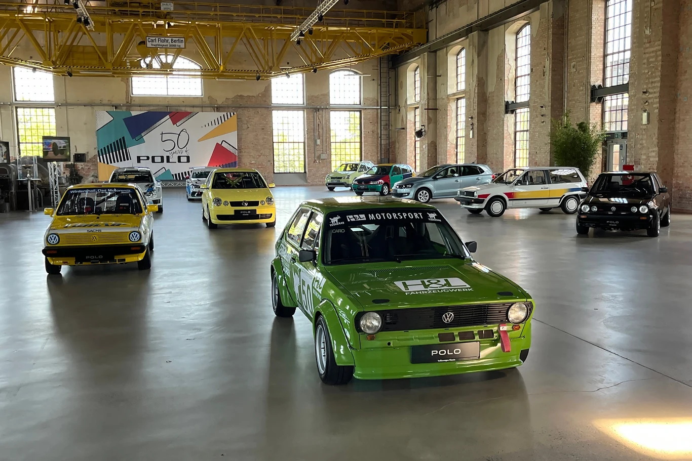 Volkswagen umożliwił nam bezpośredni kontakt z każdą generacją modelu Polo. Zabytkowe modele samochodów VW Polo są ustawione w dużej, jasnej hali wystawowej. Można dostrzec różnorodne wersje kolorystyczne i style samochodów, a w tle widnieje plakat z napisem '50 lat Polo' oraz motywami graficznymi.