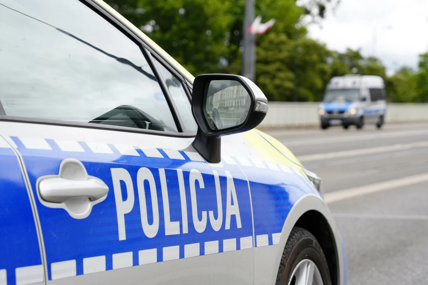Areszt tymczasowy dla podejrzanego ws. 11-latki poszukiwanej Child Alertem Radiowóz policyjny z widocznym napisem 'Policja' zaparkowany przy krawężniku drogi. W tle na ulicy jedzie policyjna furgonetka.