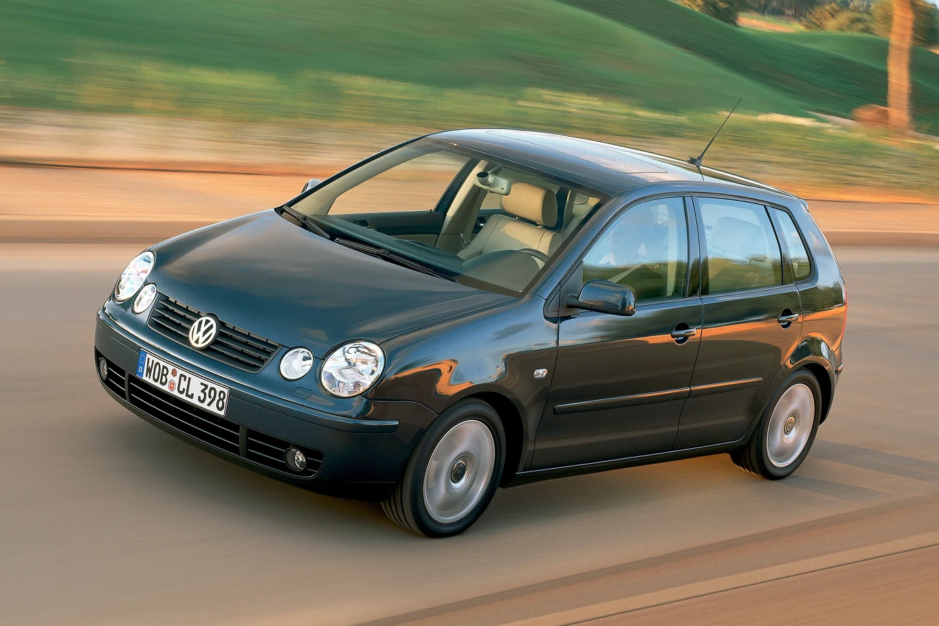 VW Polo generacji IV to przede wszystkim nowa stylistyka z zespołem czterech reflektorów. Volkswagen Polo w ruchu, czarna karoseria, niemiecka rejestracja, asfaltowa droga, tło rozmyte przez prędkość.