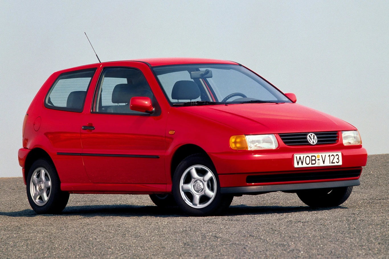 Trzecia generacja Volkswagena Polo została całkowicie przeprojektowana pod względem stylistycznym i technicznym. Czerwony samochód marki Volkswagen Polo z charakterystycznymi żółtymi reflektorami, umieszczony na asfaltowej nawierzchni. Pojazd posiada tablicę rejestracyjną WOB-V 123 i jest widoczny z prawej strony.