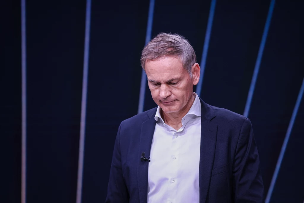 Prezes Volkswagena i Porsche OIiver Blume zmaga się z krytyką Mężczyzna w garniturze z opuszczoną głową, na ciemnym tle z jasnymi liniami. Na klapie kołnierza ma zamocowany mikrofon. Postawa sugeruje zamyślenie lub skupienie.