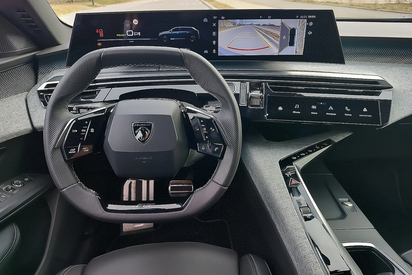 Cały kokpit Peugeota e-5008 wygląda futurystycznie Wnętrze luksusowego samochodu z nowoczesnym panelem sterowania. Widoczna kierownica ze specjalistycznymi przyciskami oraz cyfrowy wyświetlacz pokazujący informacje o pojeździe. Deska rozdzielcza ma minimalistyczny, elegancki design.