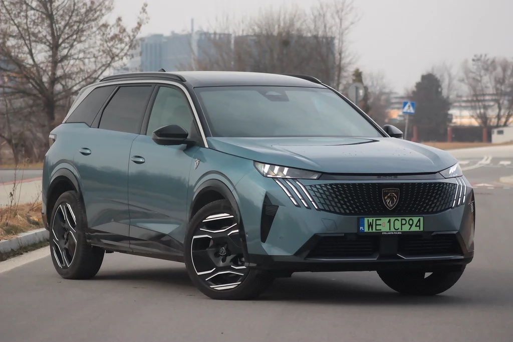 Peugeot e-5008 Współczesny SUV o eleganckiej sylwetce zaparkowany na miejskiej drodze, z charakterystycznym designem przednich świateł i logiem producenta na masce.