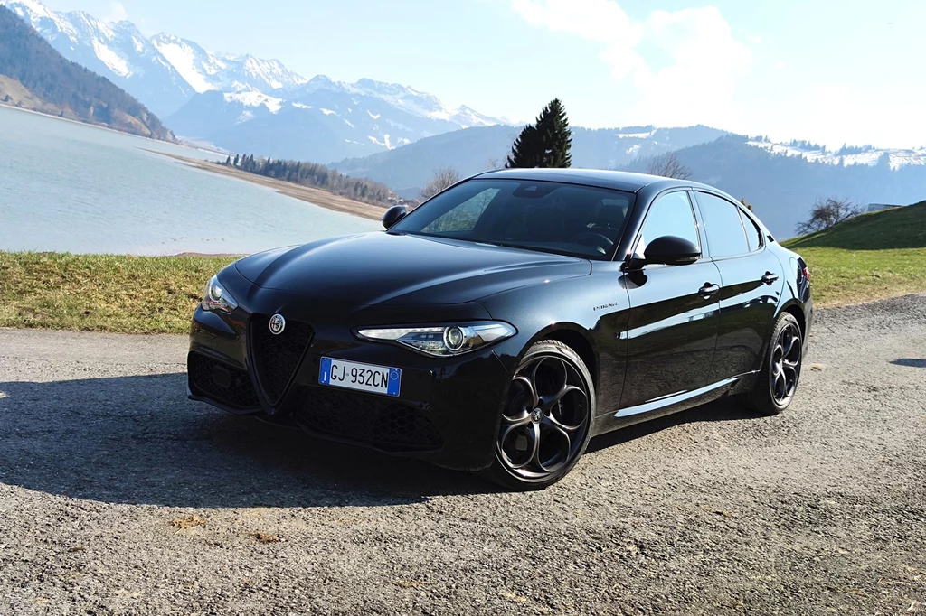 Czarna Alfa Romeo Giulia na włoskiej autostradzie może zwiastować kłopoty. Nowoczesny, czarny samochód osobowy marki Alfa Romeo zaparkowany na żwirowej drodze. W tle malownicza sceneria gór i jeziora, co nadaje zdjęciu luksusowy i elegancki wygląd.