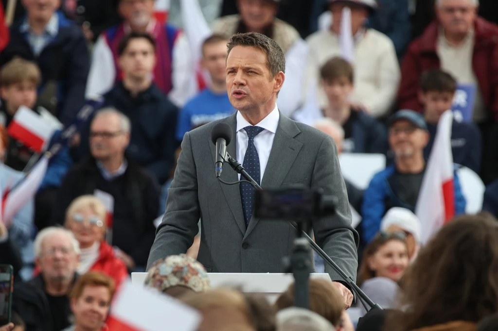 Rządzący pokładają ogromne nadzieje w zwycięstwie Rafała Trzaskowskiego w drugiej turze Mężczyzna w garniturze przemawia na wiecu. Za nim widoczny tłum ludzi, z których niektórzy trzymają flagi i plakaty. W tle widać publiczność słuchającą wystąpienia.