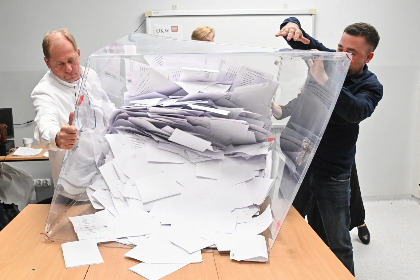 Frekwencja w wyborach prezydenckich 2025 nie zawiodła. Poznaj rekordy z poprzednich lat Osoby opróżniające przezroczystą urnę wyborczą pełną kart do głosowania na stole w pomieszczeniu. Widoczna jest tablica w tle.