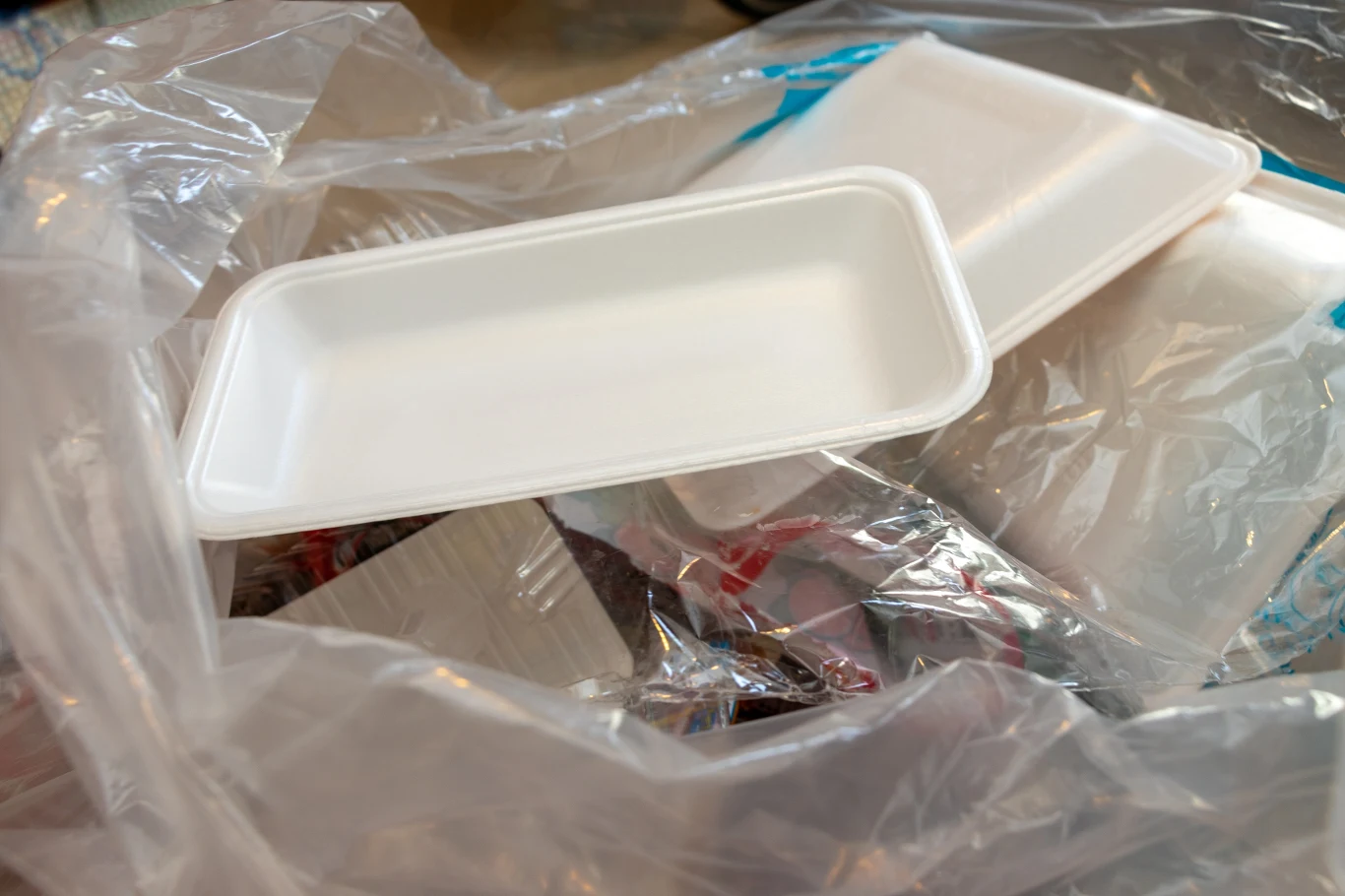 Opakowania po mięsie należy najpierw przepłukać i oczyścić z mięsnych odpadów Plastikowa tacka leży na stosie foliowych opakowań. Element centralny to biała tacka, która jest pustą, prostokątną formą na tle przezroczystych i niebieskich foliowych torebek. Scena nawiązuje do tematyki recyklingu i odpadów z tworzyw sztucznych.