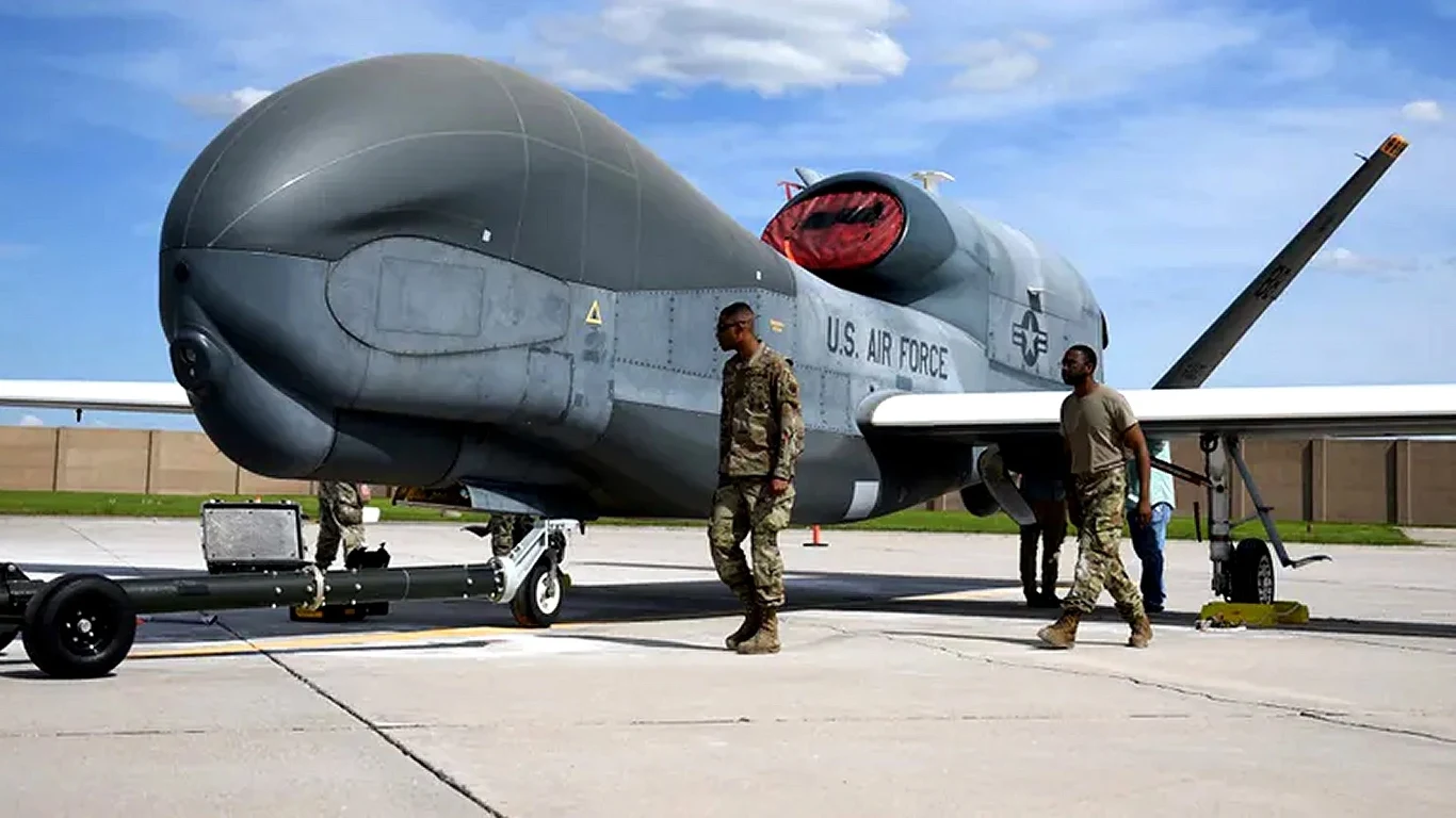 Amerykańskie drony Global Hawk pojawiły się nad Morzem Czarnym Bezzałogowy samolot wojskowy U.S. Air Force stoi na lotnisku. Obok niego znajdują się dwaj żołnierze w mundurach, patrzący na przód pojazdu. Pogodny dzień i niebieskie niebo w tle.