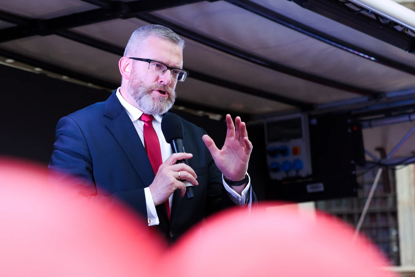 Grzegorz Braun zajął czwarte miejsce w wyborach prezydenckich Mężczyzna w garniturze i czerwonym krawacie przemawia do mikrofonu, wykonując gest ręką. Tło jest rozmyte, zawiera elementy techniczne.