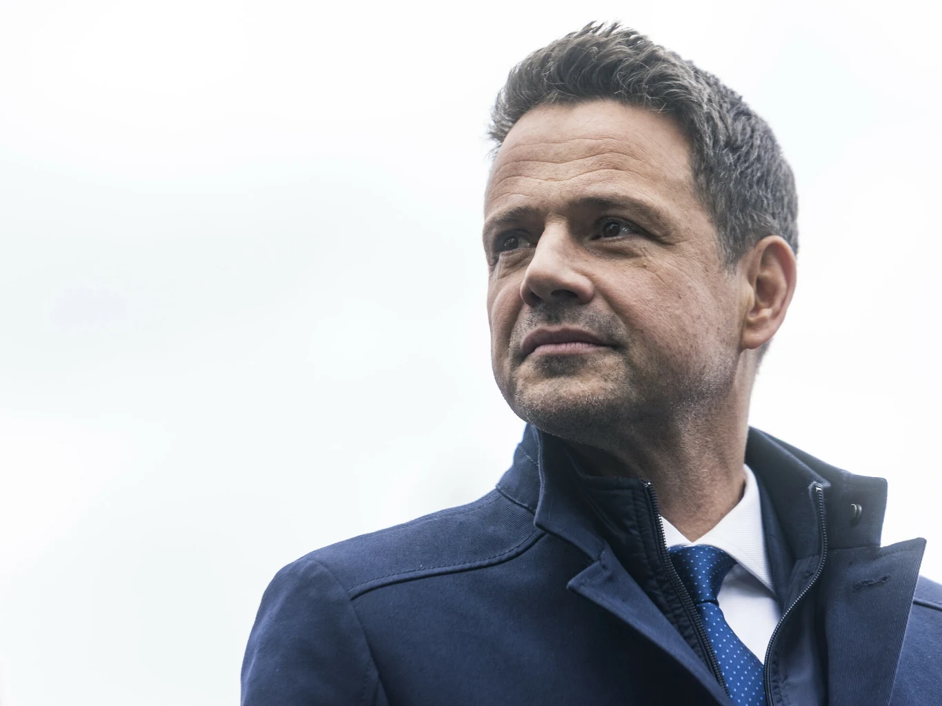 Komitet Trzaskowskiego złożył protest wyborczy Mężczyzna w średnim wieku w ciemnym płaszczu i krawacie, patrzący w dal. Jego twarz wyraża zdecydowanie i pewność siebie. Tło jest jasne i rozmyte, co nadaje zdjęciu profesjonalny wygląd.