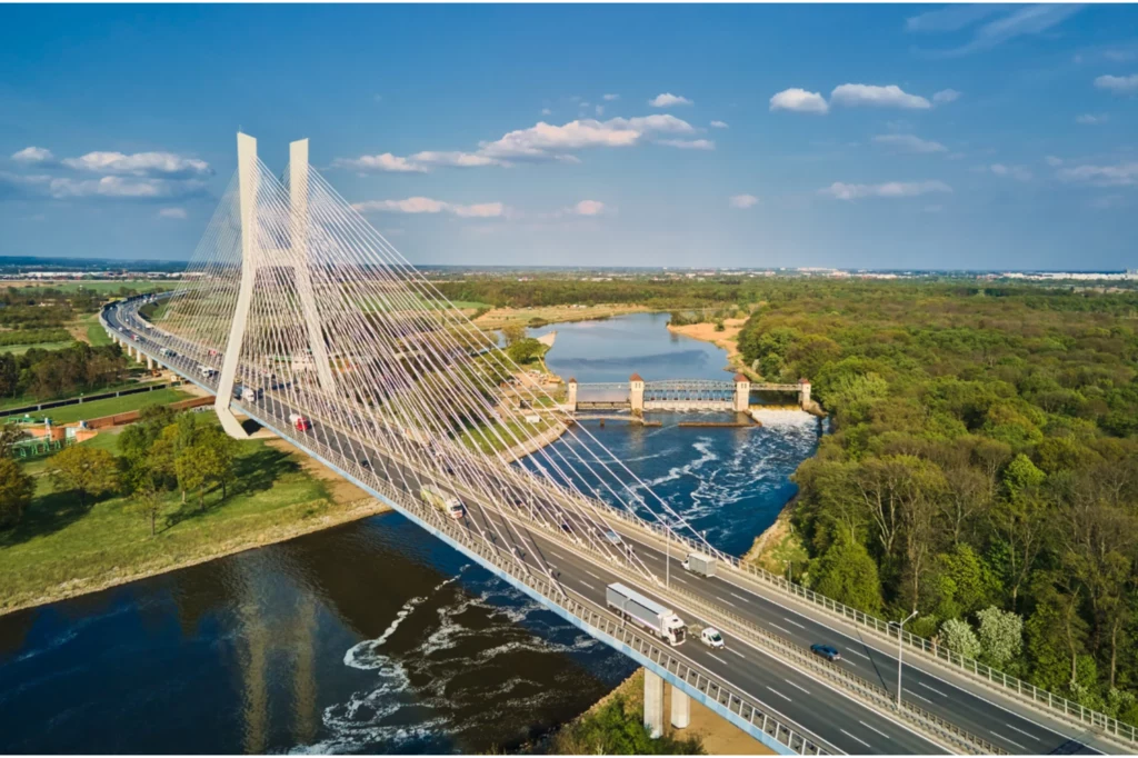 Most Rędziński we Wrocławiu uplasował się na 3. pozycji. Most wantowy nad szeroką rzeką otoczony zielonym lasem, widok z lotu ptaka. Równolegle do mostu biegnie droga z poruszającymi się pojazdami, a w tle widać spokojny krajobraz wiejski.