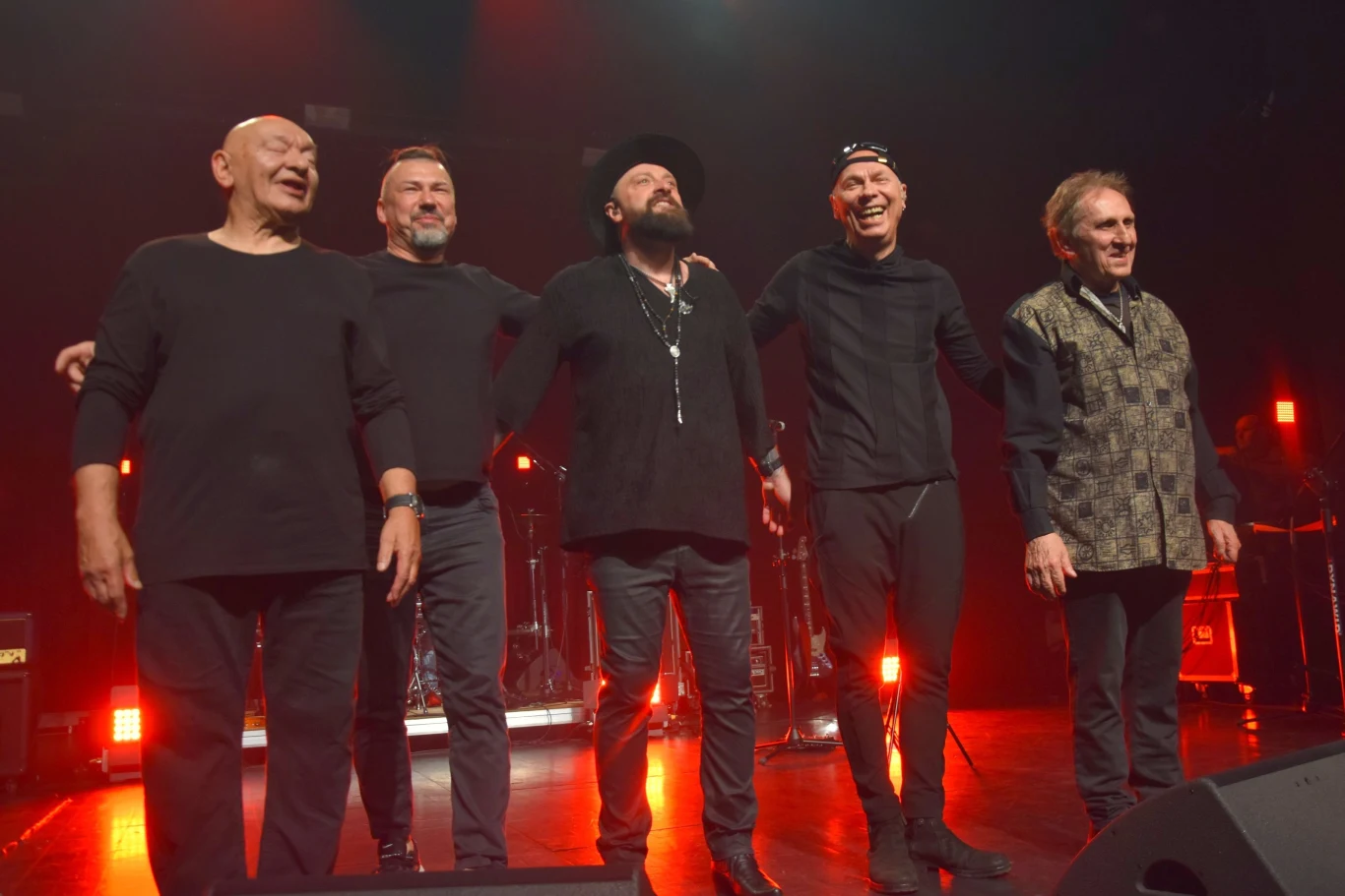 Perfect & Łukasz Drapała na pierwszym koncercie - od lewej: Darek Kozakiewicz, Krzysztof Patocki, Łukasz Drapała, Piotr Urbanek i Jacek Krzaklewski Grupa pięciu mężczyzn na scenie, obejmujących się z uśmiechami na twarzach, w otoczeniu czerwonego oświetlenia. Wszyscy ubrani są na czarno, a scena jest wyraźnie związana z występem muzycznym.