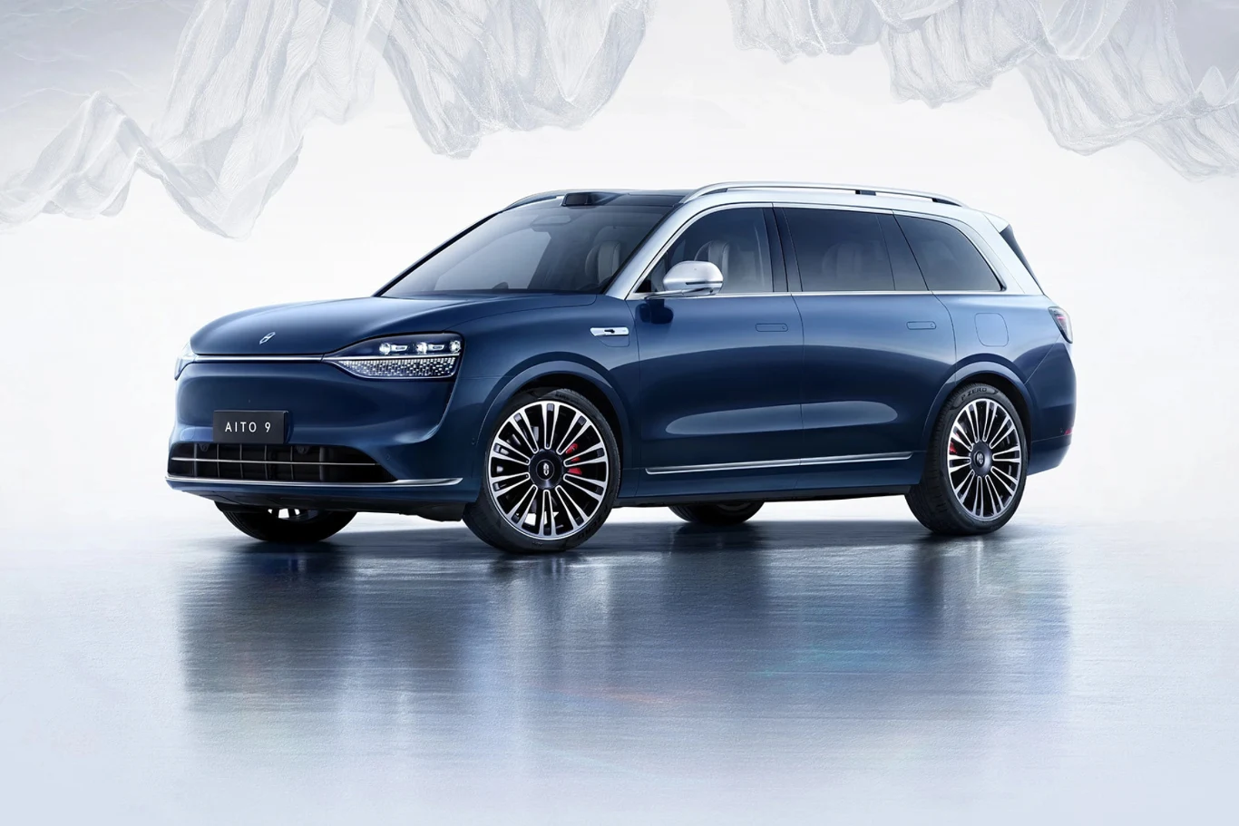 Niebieski samochód SUV na tle jasnego wnętrza z białymi falistymi elementami dekoracyjnymi. Pojazd posiada elegancki design z nowoczesnymi reflektorami i dużymi kołami, co podkreśla jego luksusowy charakter.