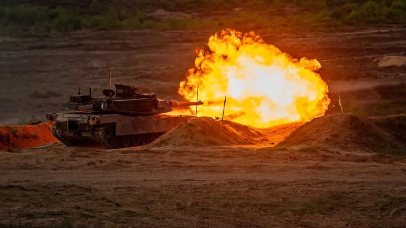 Polskie Abramsy ruszyły na ćwiczenia. Pokazano zdjęcia z prób ogniowych Czołg strzelający na poligonie, z dużym wybuchem ognia i dymem. W tle rozległy, pusty teren, co sugeruje ćwiczenia wojskowe.