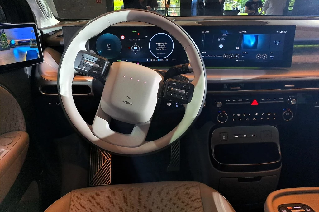 Hyundai Ioniq 9 oferuje kokpit wyposażony w zakrzywiony zestaw ekranów, na które składają się dwa 12-calowe wyświetlacze. wnętrze nowoczesnego samochodu elektrycznego z dużym ekranem dotykowym, minimalistyczną kierownicą oraz cyfrowym kokpitem. Ekrany wyświetlają różne informacje takie jak prędkość i mapy nawigacji