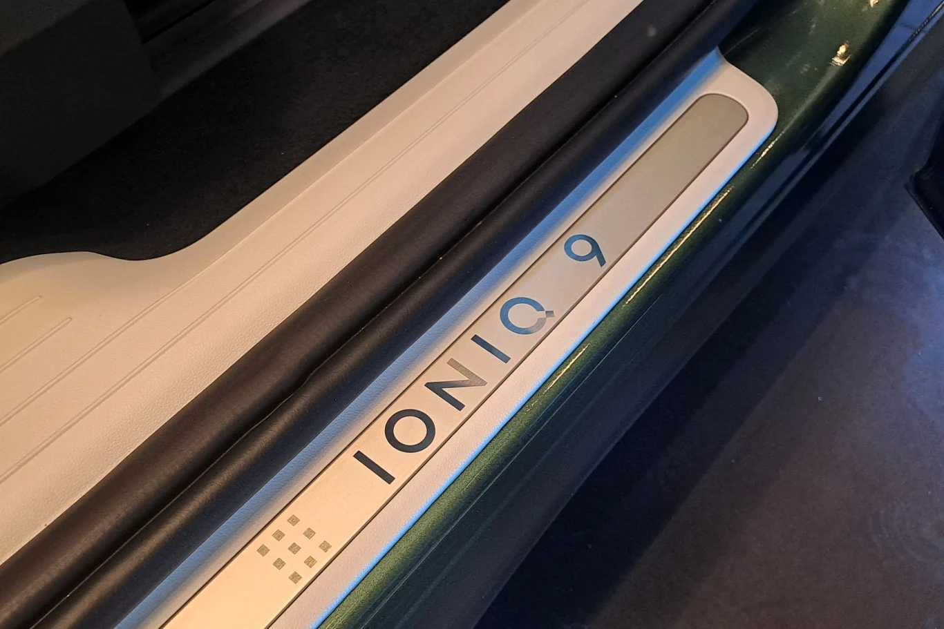 Próg samochodu z napisem 'IONIQ 9' z widocznym stylowym wykończeniem, znajdujący się w przestrzeni przy drzwiach auta. Wygląda na elegancko wykończony z nowoczesnym wyglądem.
